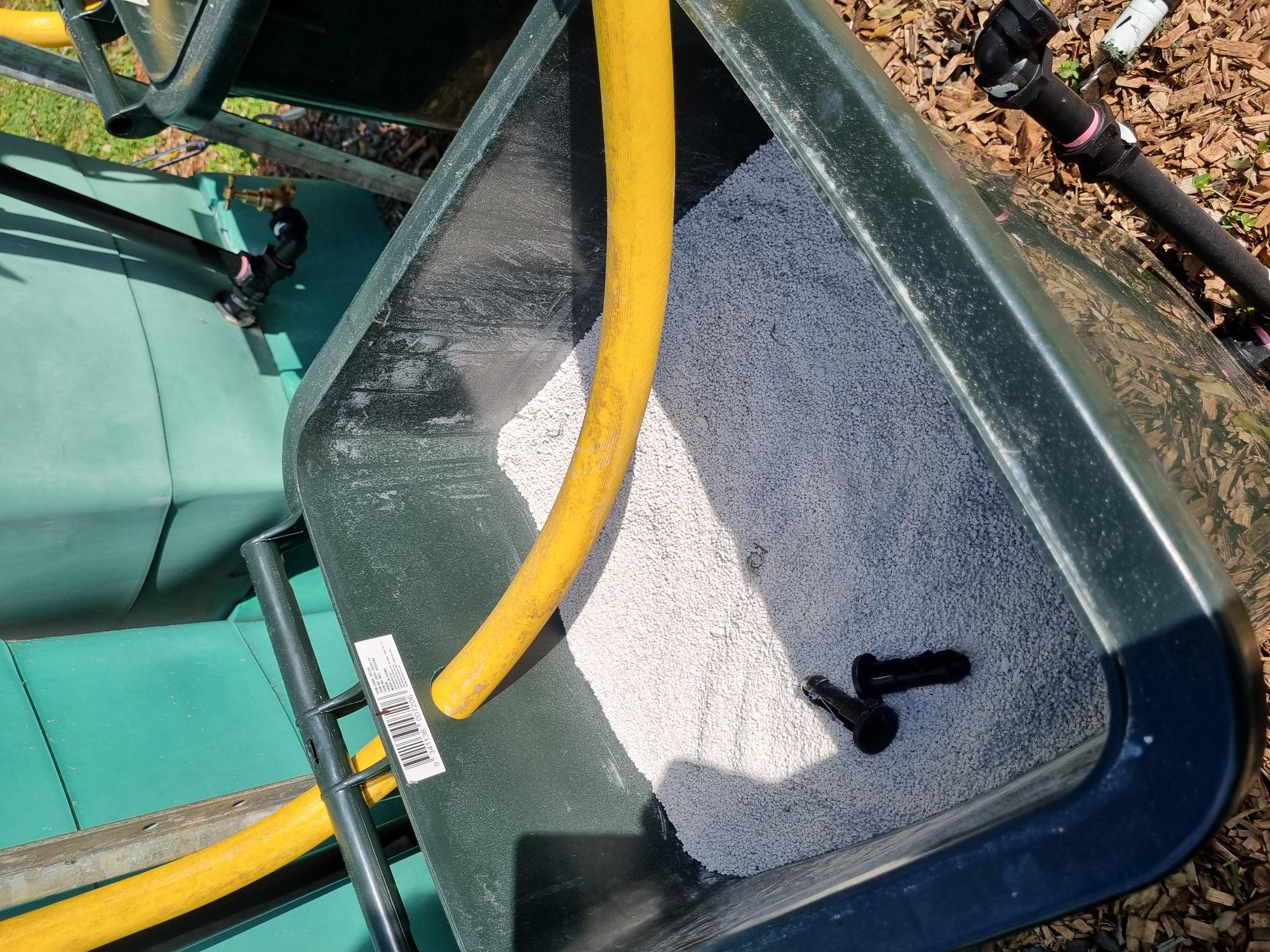 Image shows the opening of a green bin, looking down into the bin.  The bin is full of white sandy material.  A yellow pipe is inserted into the top of the back of the bin.