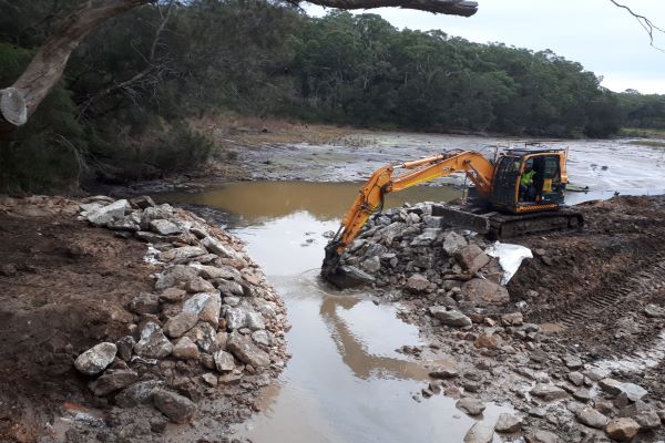 Excavator working on rocks within waterway