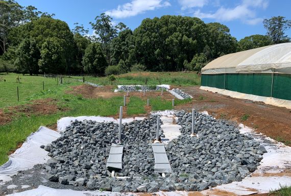 Pipes, buried under rocks, in a grassy area next to a greenhouse 